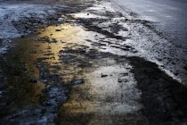Huella de rueda en camino de asfalto con nieve fangosa derretida en el crepúsculo - foto de stock