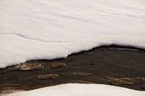 Tauloch in schmelzender Eisschicht mit schneebedecktem Wasserstrom im Frühling — Stockfoto