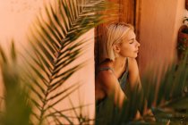 Молодая женщина с закрытыми глазами сидит возле деревянных дверей и растений во дворе — стоковое фото