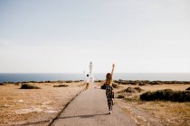 Happy lovers jumping with arms raised on path to lighthouse — Stock Photo