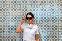 Belle femme en tenue décontractée et écouteurs avec debout sur le mur de mosaïque bleue du bâtiment sur la rue de la ville — Photo de stock