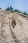 Знизу людина піднімається на скелю в природі з обладнанням для скелелазіння — стокове фото