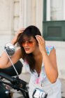 Mujer de moda de confianza peinado peinado, mientras que de pie y admirándose en el espejo de la motocicleta en la calle - foto de stock