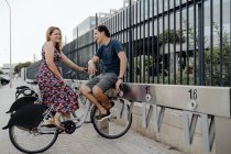 Side view of romantic couple talking tenderly while sitting on bicycle and having rest nearby ornamental fence during walking — Stock Photo