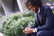 Joyful african american man in suit sitting outside and messaging — Stock Photo
