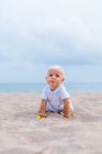 Vista frontal de un bebé rubio en la playa - foto de stock
