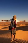 Unrecognizable tourist with outstretched arms standing against bright cloudless sundown sky in desert — Stock Photo