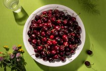 Vista superior de cerejas doces frescas na tigela na toalha de mesa verde — Fotografia de Stock