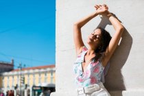 Peaceful gorgeous woman in trendy outfit standing on white wall with hands up on scenic street — Stock Photo