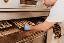 Взрослый человек с избыточным весом заглядывает внутрь профессиональной печи во время работы в пекарне — стоковое фото