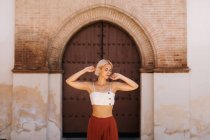 Приваблива молода жінка в стильному вбранні складні руки і закриті очі, стоячи навпроти стародавньої будівлі з міцними воротами на вулиці старого міста — стокове фото
