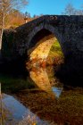 Старий кам'яний міст над спокійною річкою в сонячний день в мальовничій осінній сільській місцевості — стокове фото