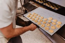Человек на полях заглядывает внутрь профессиональной печи во время работы в пекарне — стоковое фото