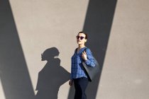 Manager in sunglasses and elegant outfit smiling and looking at camera while standing against gray building wall on city street — Stock Photo