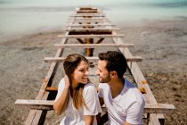 Glad lovers sitting on destroyed pier on seashore — Stock Photo