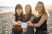 Trois jolies femmes serrant une carte devant la caméra avec le soleil derrière elles — Photo de stock