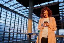 Smiling young woman browsing phone at station — Stock Photo