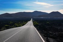 Svuota strada curva a piedi a valle di montagna lungo il campo scuro con vegetazione a Lanzarote Isole Canarie Spagna — Foto stock