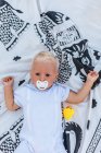 Vista superior de un bebé rubio con chupete en una manta - foto de stock