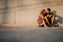 Hombre y mujer mirándose unos a otros y abrazándose sentados en la pared cercana de la calle. - foto de stock