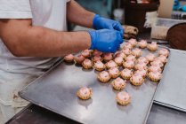 Unrecognizable confectioner decorating pink pastry on tray while working in bakery — Stock Photo