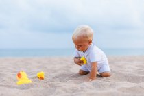 Porträt eines Jungen, der mit Gummienten am Strand spielt — Stockfoto