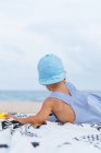 Visão traseira de um bebê com um boné na praia ao lado de seus patos de borracha — Fotografia de Stock
