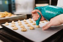 Anonyme Köchin drückt frischen Teig auf Blech mit Papier, während sie an verschwommenem Hintergrund der Bäckerei arbeitet — Stockfoto