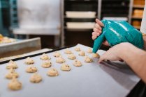 Анонімний кухар стискає свіже тісто для випічки на підносі з папером, працюючи на розмитому фоні пекарні — стокове фото