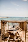 Лодка пришвартована на берегу под деревянным навесом на песчаном пляже в летний солнечный свет — стоковое фото