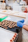 Unrecognizable confectioner decorating pink pastry on tray while working in bakery — Stock Photo