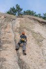 Снизу человек карабкается по скале на природе с альпинистским снаряжением — стоковое фото