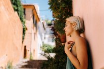 Seitenansicht der schönen jungen Frau mit kurzen blonden Haaren, die die Augen schließt und sich auf der Straße an die Wand lehnt — Stockfoto
