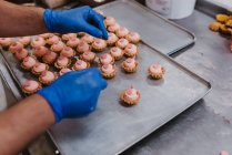 De dessus confiseur méconnaissable décorer pâtisserie rose sur plateau tout en travaillant dans la boulangerie — Photo de stock