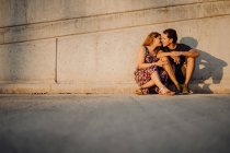 Mann und Frau schauen einander an und küssen sich, wenn sie an der nahen Straßenmauer sitzen — Stockfoto