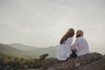 Feliz pareja sentada en el acantilado de las montañas - foto de stock