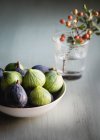 Des figues colorées mûres vertes et pourpres dans un bol sur une table en bois à côté de baies brillantes. — Photo de stock