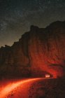 Véhicule stationné près de falaise rugueuse pendant le voyage à travers le désert de Wadi Rum à la nuit étoilée en Jordanie — Photo de stock