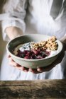 Hands of woman holding bowl with delicious crispy granola served with fresh berries, yogurt and chia seeds — Stock Photo