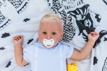 Vista superior de un bebé rubio con chupete en una manta - foto de stock