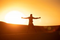 Вид ззаду на невпізнаваного туриста з простягнутими руками, що стоять на тлі яскравого безхмарного сонячного неба в пустелі — стокове фото
