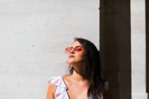 Mulher linda pacífica na roupa da moda e óculos de sol brilhantes em pé na parede branca na rua cênica — Fotografia de Stock