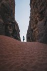 Anonimo turista donna in piedi sulla sabbia tra muri di pietra grezza contro cielo blu senza nuvole nel burrone del deserto Wadi Rum in Giordania — Foto stock