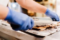 Anonyme Köchin in Handschuhen schneidet leckeren Schichtkuchen auf Tisch in Backküche — Stockfoto