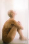 Vue latérale de la jeune femme prenant une douche derrière cloison transparente humide dans la salle de bain — Photo de stock