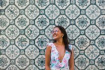 Friedliche, hinreißende Frau im trendigen Outfit und glänzender Sonnenbrille, die neben einer gefliesten, exotischen Wand auf einer malerischen Straße steht — Stockfoto
