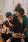 Tenera coppia allegra in abiti casual suonare la chitarra a casa — Foto stock