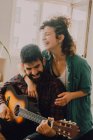 Tendre couple joyeux dans des tenues décontractées jouer de la guitare à la maison — Photo de stock