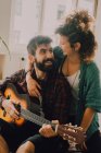 Tender cheerful couple in casual outfits playing guitar at home — Stock Photo