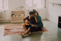 Tenera coppia allegra in abiti casual suonare la chitarra a casa — Foto stock